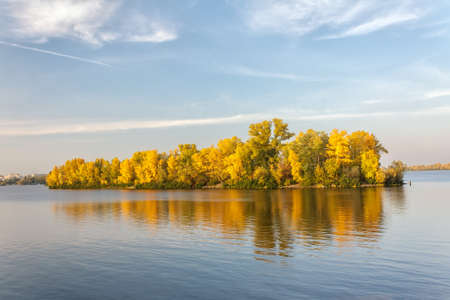 Autumn island on a river and its reflection in blue waterの写真素材