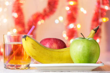 Banana, green and red apples on white plate and glass of apple juice (birthday party)の写真素材