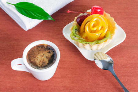 Closeup of cupcake with jelly and fruits on a white plate and a cup of coffee on a brown backgroundの写真素材
