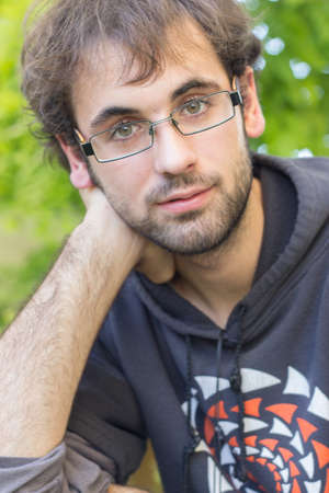 Portrait of young boy with beard and glasses, dressed in sweatshirt with drawing; In the field, outdoors. Selective focusの写真素材