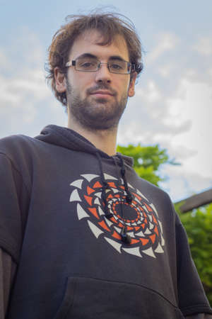 Portrait of young boy with beard and glasses, dressed in sweatshirt with drawing; In the field,...