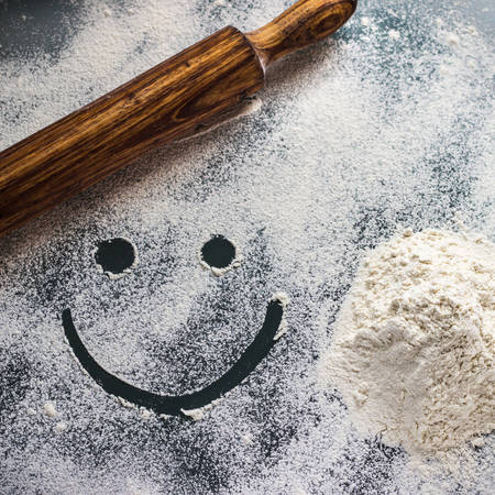 wheat flour on work table with smiley and wooden rollerの写真素材