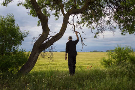 Farmer on his back looking at the field on a cloudy dayの写真素材