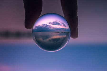Sunset seen in a crystal ball. Jetty on a quiet beach with clouds and blue skyの写真素材