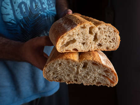 Baker man holding rustic loaf of wheat bread in hands.