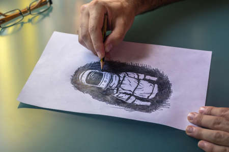 Man's hands drawing in pencil an astronaut on a green glass table, with some glasses on the table. Concept of art.の写真素材