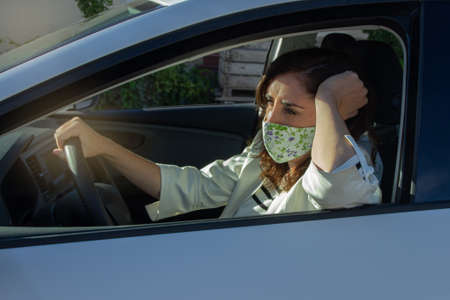 Senior Hispanic woman with face mask driving her car with her arm leaning on the window.の写真素材