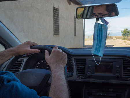 man driving through the field with the mask hanging on the rear view mirror and latex gloves for the...