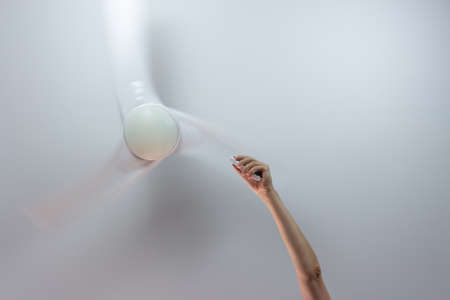 Close-up of hand holding remote control of white ceiling fan.