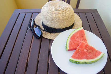 plate with watermelon slices, hat and sunglasses on a terrace table. Summer concept. Selective focus.の写真素材