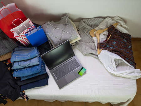 Vertical view of a bed full of clothes with a laptop computer and a credit card. Internet shopping...