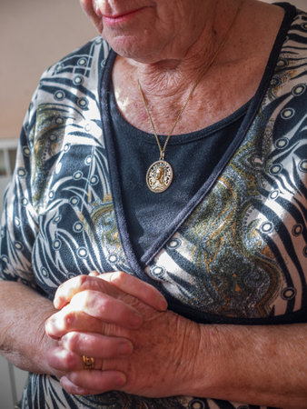 Unrecognizable older woman praying with linked hands and a gold medallion with the Virgin hanging around her neck. Concept of Christianityの写真素材