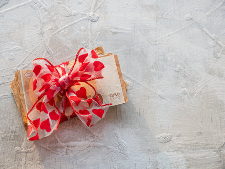 Wad of 50 euro banknotes wrapped as a gift with a red bow of hearts with space for copy. Currency concept.の写真素材