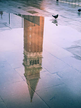 Reflection on a puddle of the bell tower of the church of San Marco, Campanille, Venice, Italy with pigeons.の写真素材