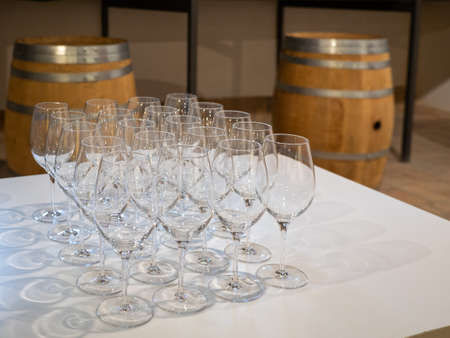 sparkling crystal wine glasses arranged in a row on a table with a white tablecloth ready for wine tasting, matrix, wine barrel in backgroundの写真素材