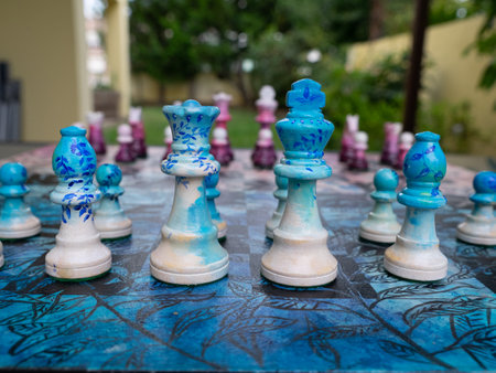 Chess board decorated in pink and blue with the pieces ready to play a game in a garden. The king and queen defended by pawns and bishop.の写真素材