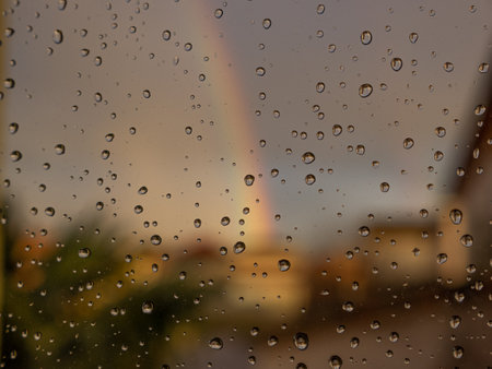 Rainy Day Concept In The Small Town. Rainbow Outside Of Home. Water Droplet Texture Background, Rain Drops on Glass Windowの写真素材