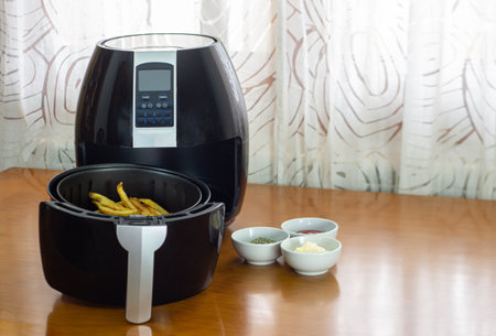 Air fryer with French fries on a table with sauces and spices. healthy food conceptの写真素材
