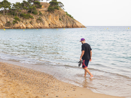 Young man walking on the beach with shoes in hand. Palamos, Spain. Vacation concept.の写真素材