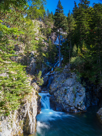 A mountain river forms waterfalls between rocks and vegetation with autumn colors.