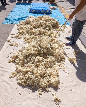 A mattress maker aerating with two sticks the wool of a mattress to make a new wool mattress.