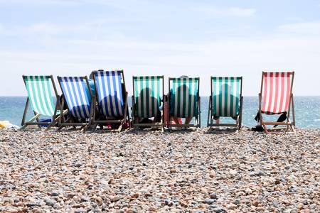 Silhouettes of people relaxing on striped deckchairs on Worthing beach, capturing a traditional English seaside view.の写真素材