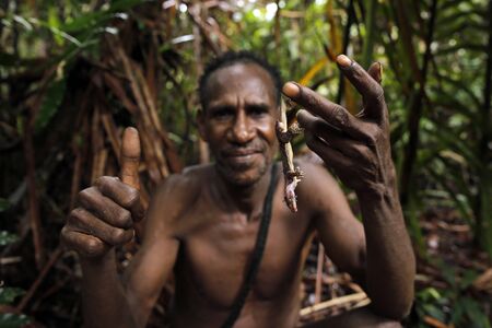 Man of the Nomadic Forest Tribe Korowai, with a Jungle Snack. West Papua, Indonesiaのeditorial素材