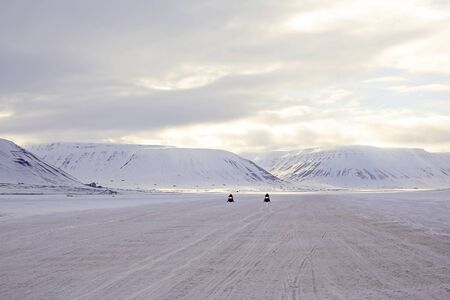 Two Snowmobiles Approaching, Snowy Mountains in the Background. Svalbard, Norwayの写真素材