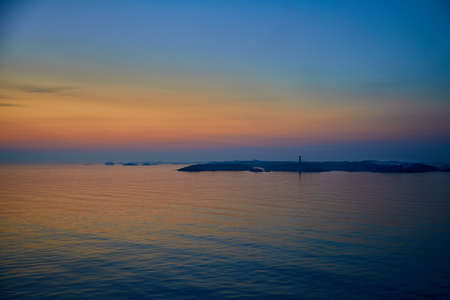 Little island with lighthouse at twilight in middle of the seaの写真素材