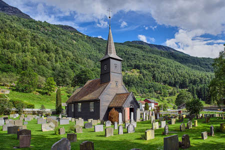 Graveyard and wooden old church with green mountains at the background in a sunny day in Flam, Norway.の写真素材