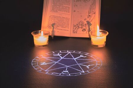 spell book with two candles on the sides and a pentacle drawn on a black background