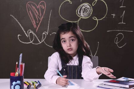 little girl doing homework at a study table with a blackboard in the background