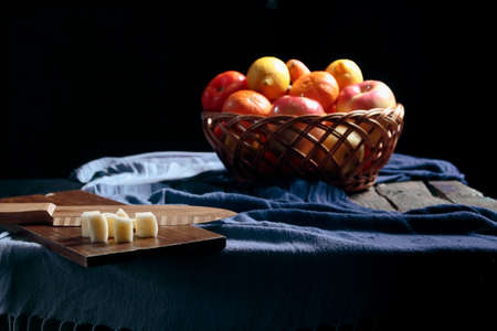 Antique wooden table with a basket full of fruit on top and a table with apple tacos and dark backgroundの写真素材