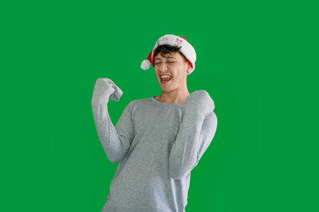 happy young man celebrating with christmas hat with green background. christmas winner concept.