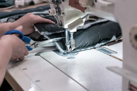 A seamstress cuts fabric while working at a sewing machine in the workshop. Women's handsの写真素材