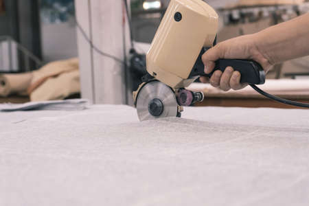 The cutter cuts the fabric with a disc cutting knife in the sewing workshopの写真素材