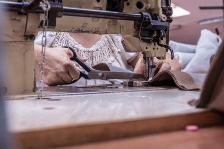 Seamstress cuts fabric while working on an old sewing machine in the workshop. Women's handsの写真素材