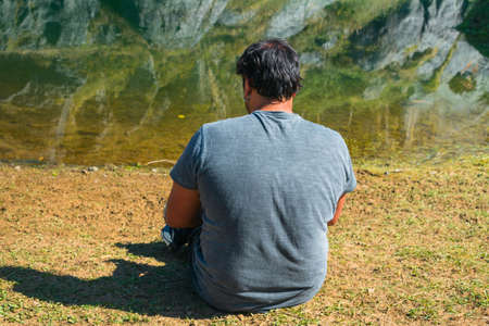 A young man sitting in front of a lake on a spring day, portrait, la arboleda, basque country