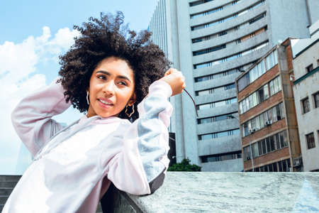 beautiful african american teenage girl with curly hair in the city with buildings behind traveling...