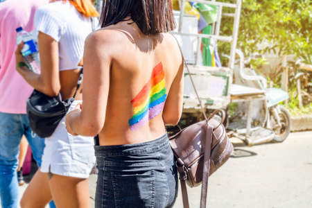 teenage woman from the back without a shirt with a painted flag of lgbt in pride on a sunny day in the cityの写真素材