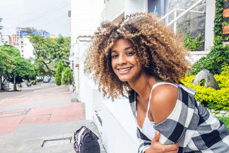 beautiful afro woman sitting in garden smiling at camera with curly brown hair, on sunny day in the...