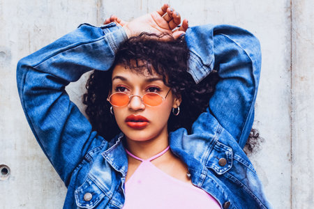closeup portrait of teen woman wearing orange glasses and blue jacket posing in city trendy looking...
