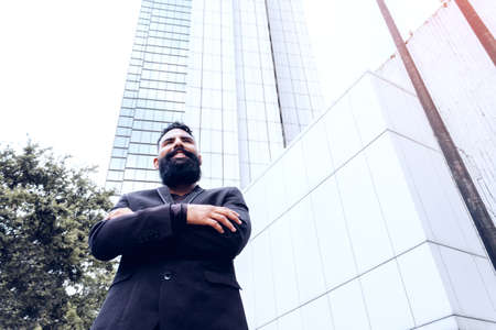 business executive man businessman in black suit caucasian with long beard crossing arms in modern building structure outdoor smiling in city.の写真素材