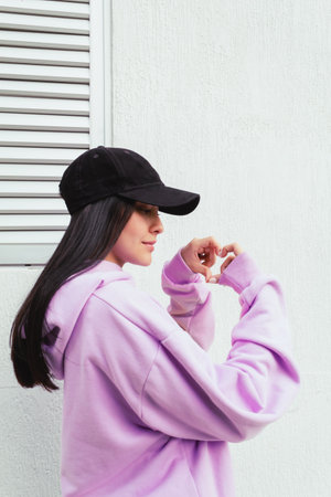 Portrait of a young woman in a pink hoodie and a black cap.