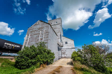 Pennant, SK, Canada- July 9, 2019: The abandoned vintage grain elevator in Battrum, Saskatchewan with a train beside itのeditorial素材