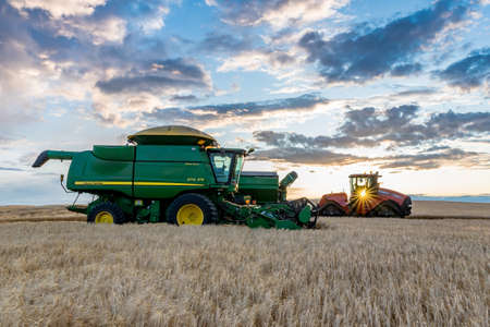 Swift Current, SK/Canada- Aug 25, 2019: Sunburst over combine and grain cart harvesting wheat in Saskatchewanのeditorial素材
