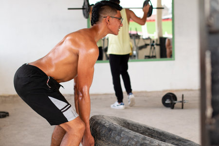 Shirtless Hispanic man lifting a tire at the gym. High quality photoの写真素材