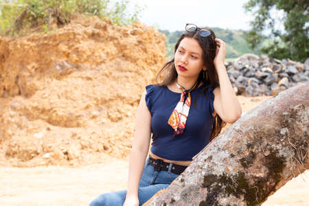 Young Latin woman in profile view. posing on a log in a deserted landscapeの写真素材