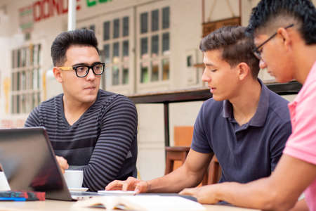 Three young people talking outdoors while using a laptop.の写真素材