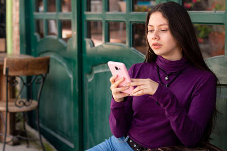 Serious woman sitting while using her smart phone in urban street.
